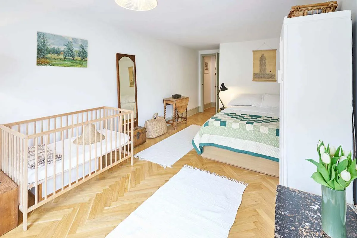 A bedroom with a bed, a wooden crib, and rugs on the floor.