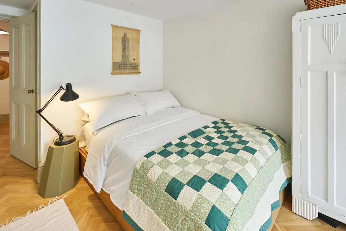 A bedroom with white bedding and a green-and-white patchwork quilt.