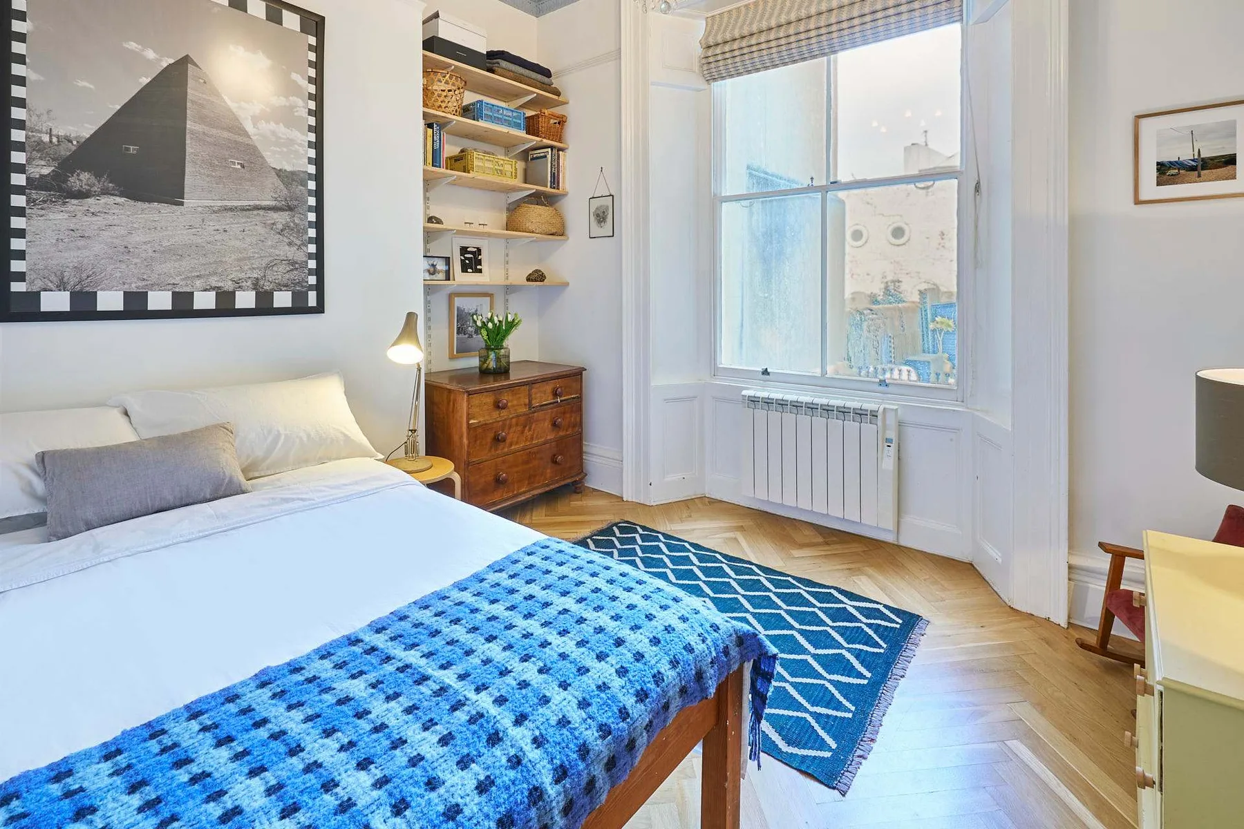 A bright bedroom with a bed, blue patterned bedding, and a large window.