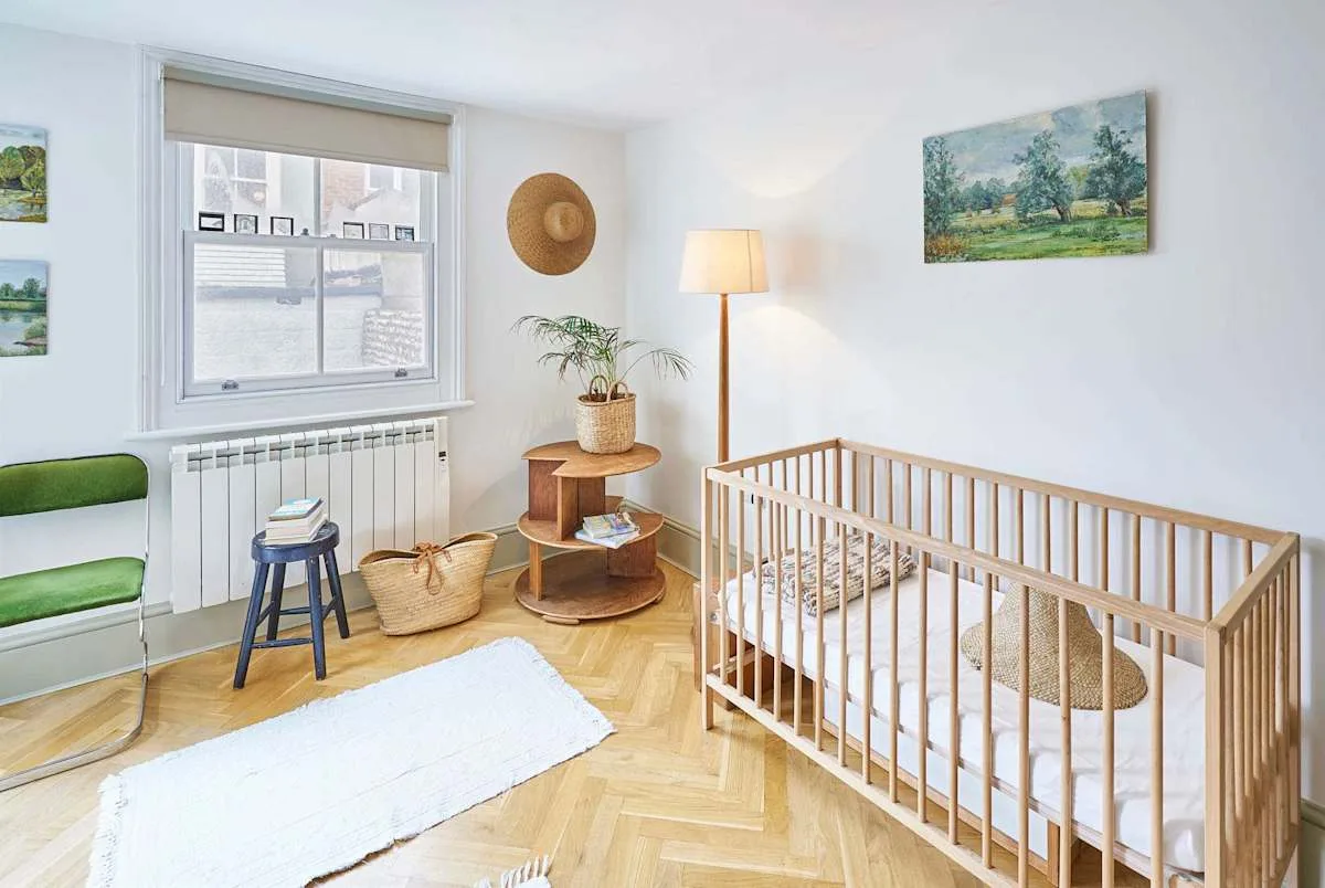 A bright room with a wooden crib, green seating, and a window.