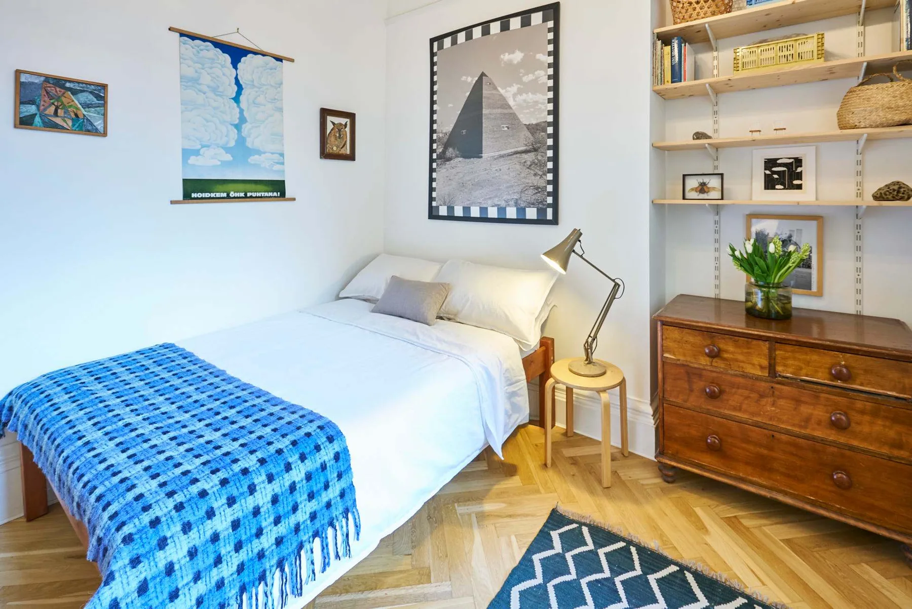A bright bedroom with a neatly made bed, bedside lamp, and wall art.