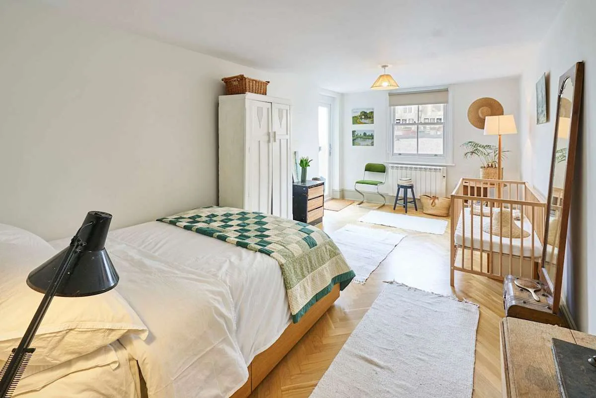 A bright bedroom with a bed, a crib, and a window seating area.