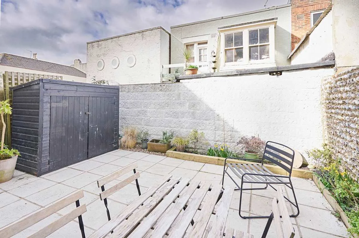 A paved patio with outdoor seating, planters, and a dark storage shed.