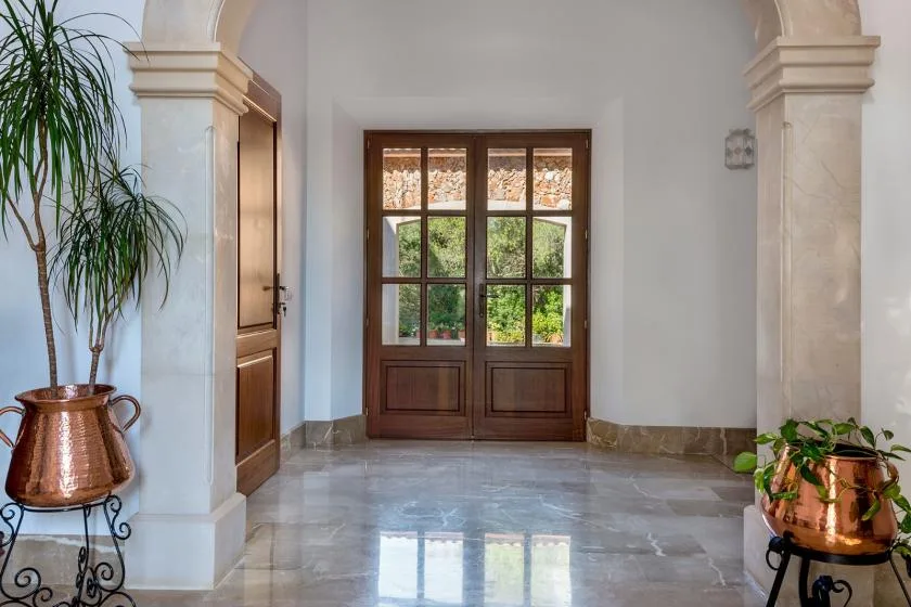 Una entrada con arco y puertas dobles de madera que dan a un jardín.