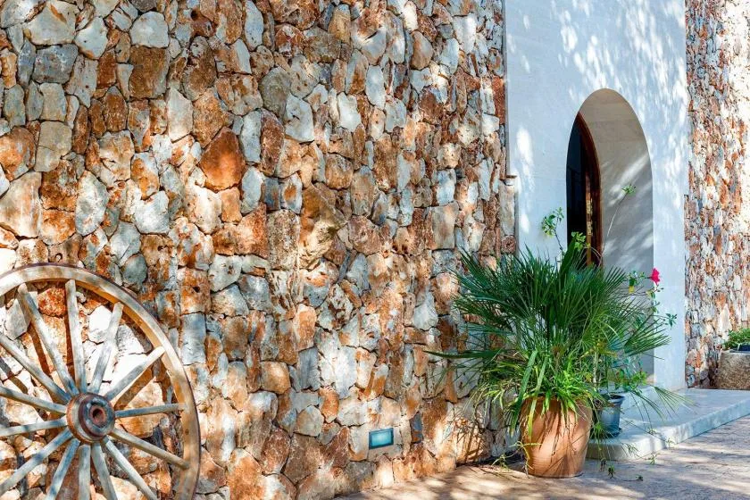 A stone exterior wall frames an arched doorway and potted greenery.