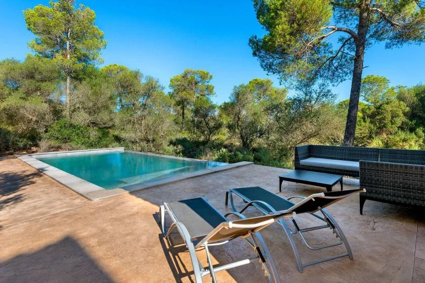 An outdoor swimming pool sits beside a paved patio with loungers and seating.