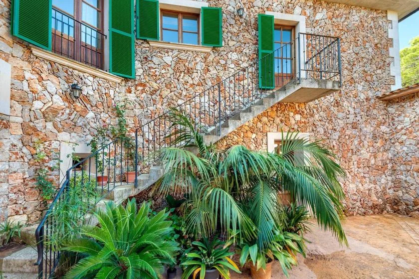 A stone building facade with green shutters, an exterior staircase, and plants.