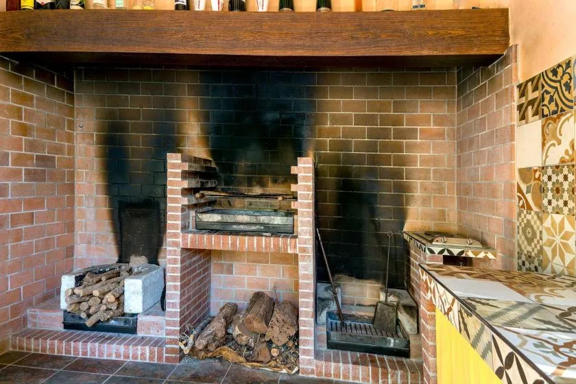 A brick fireplace with stacked firewood sits beneath a dark wooden mantel.