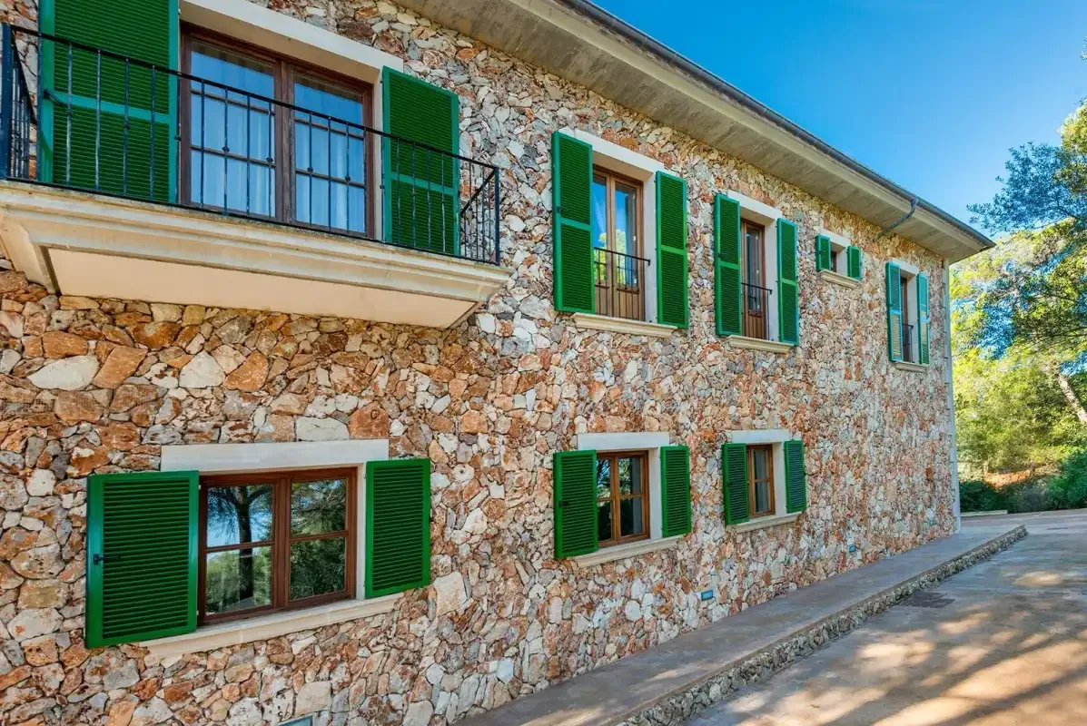 A stone-faced building with green shutters beside a paved driveway.