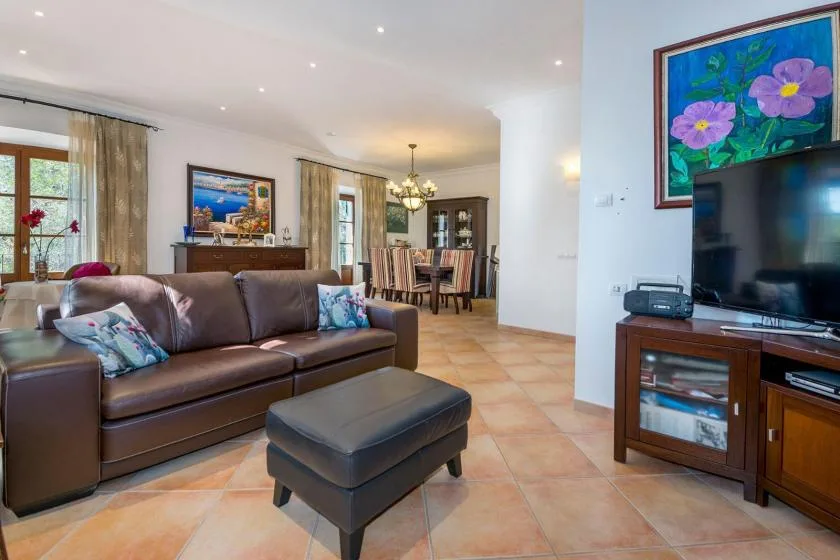 A living room with brown seating and a television beside a dining area.