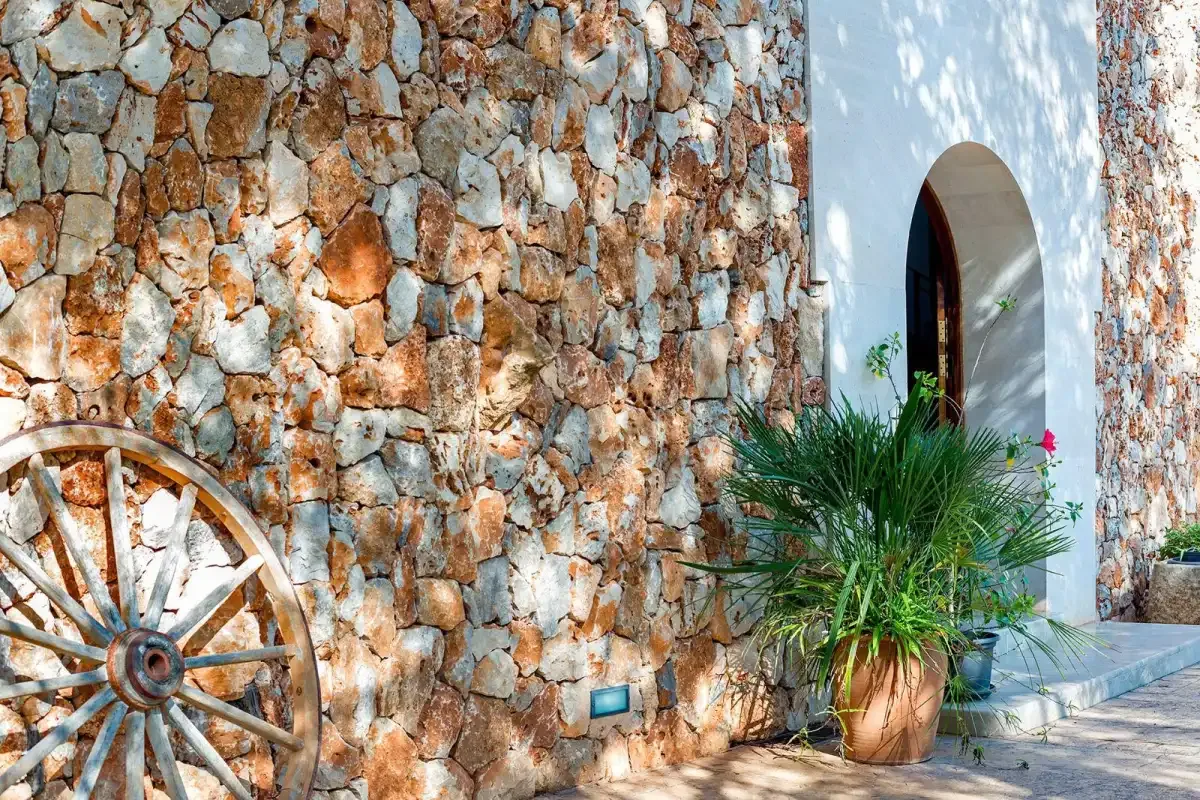 A stone exterior wall with a wooden wagon wheel beside an arched doorway.