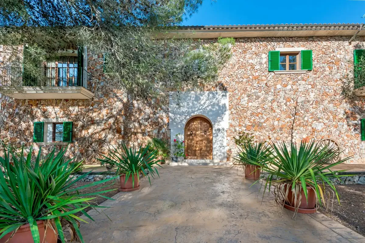 A stone house entrance opens onto a paved courtyard with potted plants.