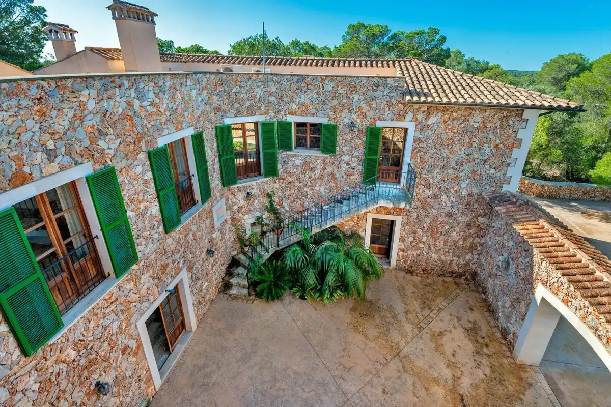 A stone courtyard sits beneath a two-story building with green shutters.