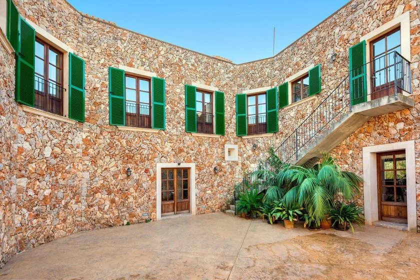 A stone courtyard with green-shuttered windows and potted palms.