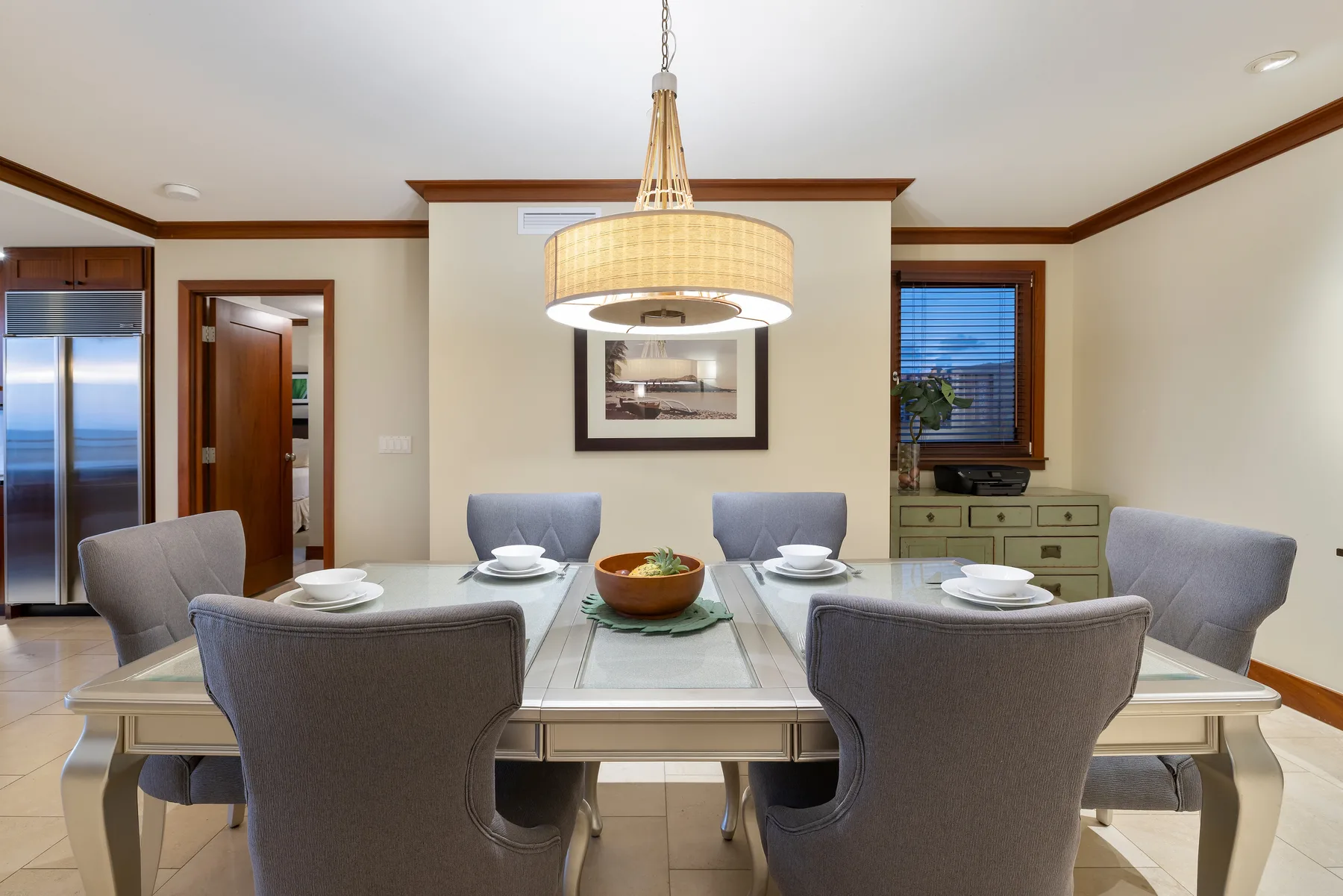 Comedor con una mesa de vidrio, asientos tapizados y una lámpara colgante.