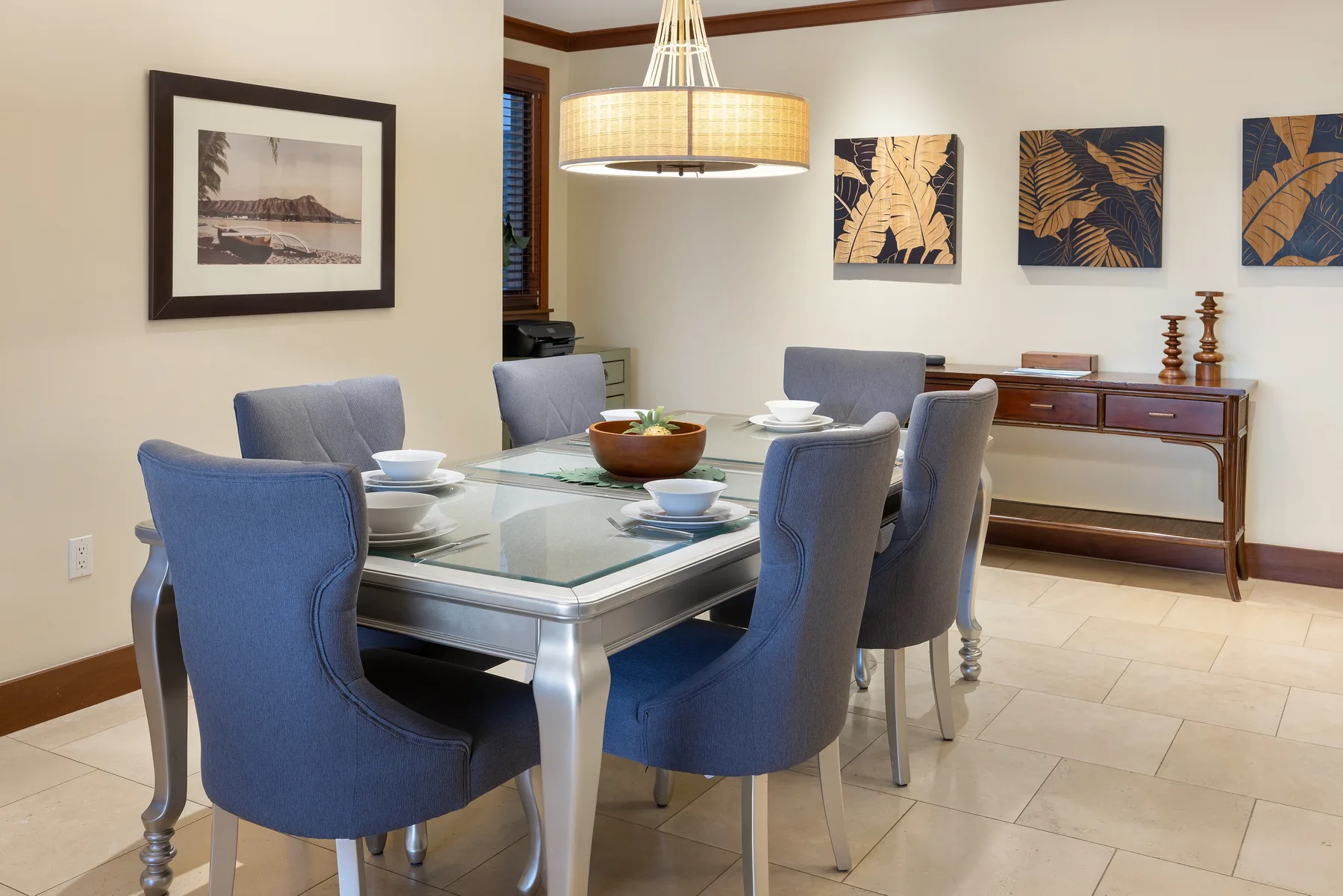 Comedor con mesa de vidrio, asientos tapizados y cuadros en la pared.