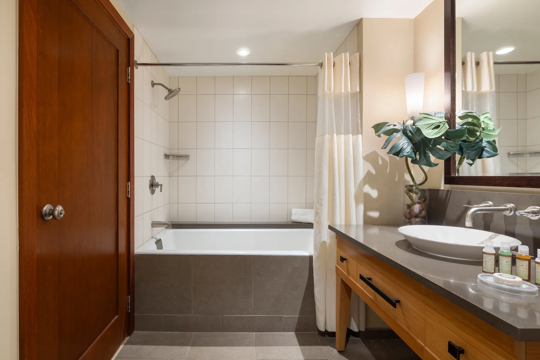 Un baño con bañera, cortina de ducha y lavabo junto a un espejo grande.