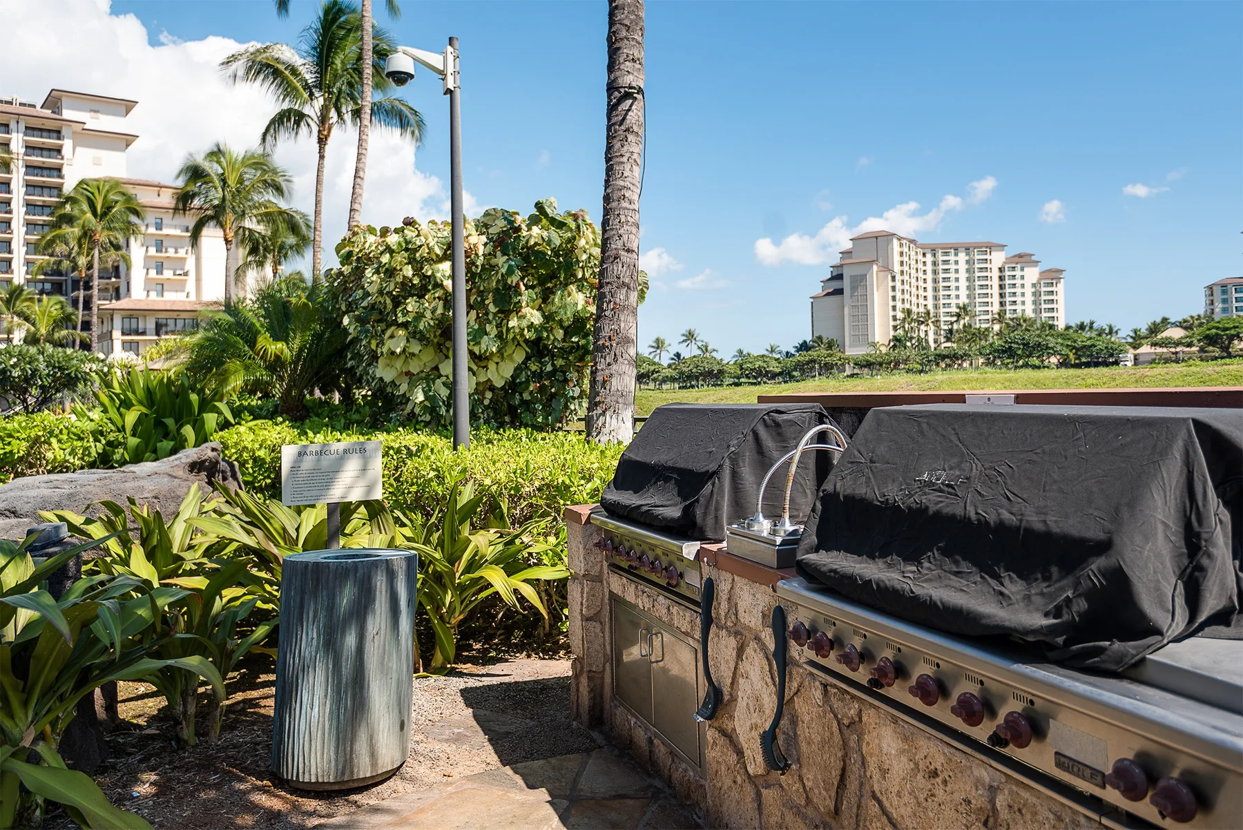 Una zona de cocina al aire libre junto a plantas tropicales, con edificios a lo lejos.