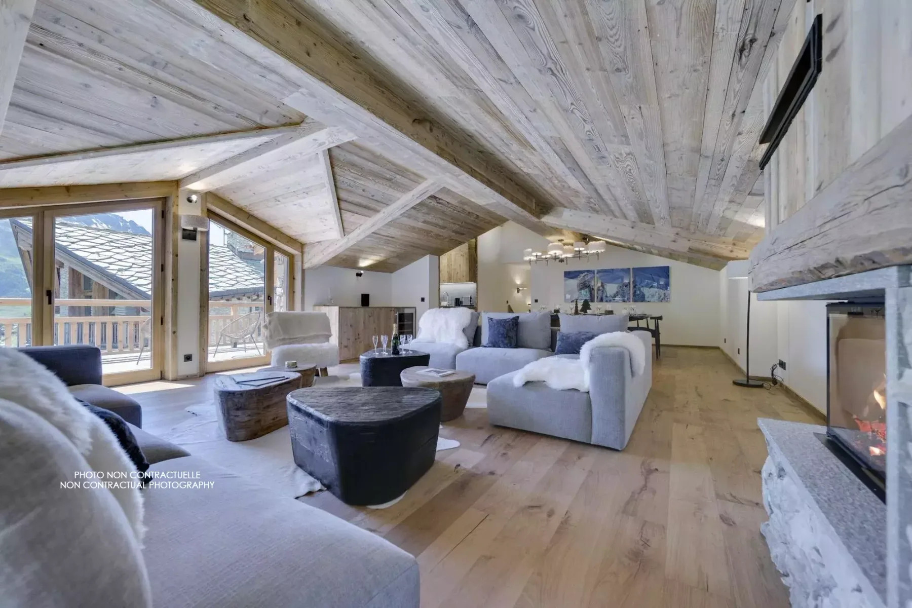 A spacious living room with seating, low tables, and large windows beneath a sloped wood ceiling.