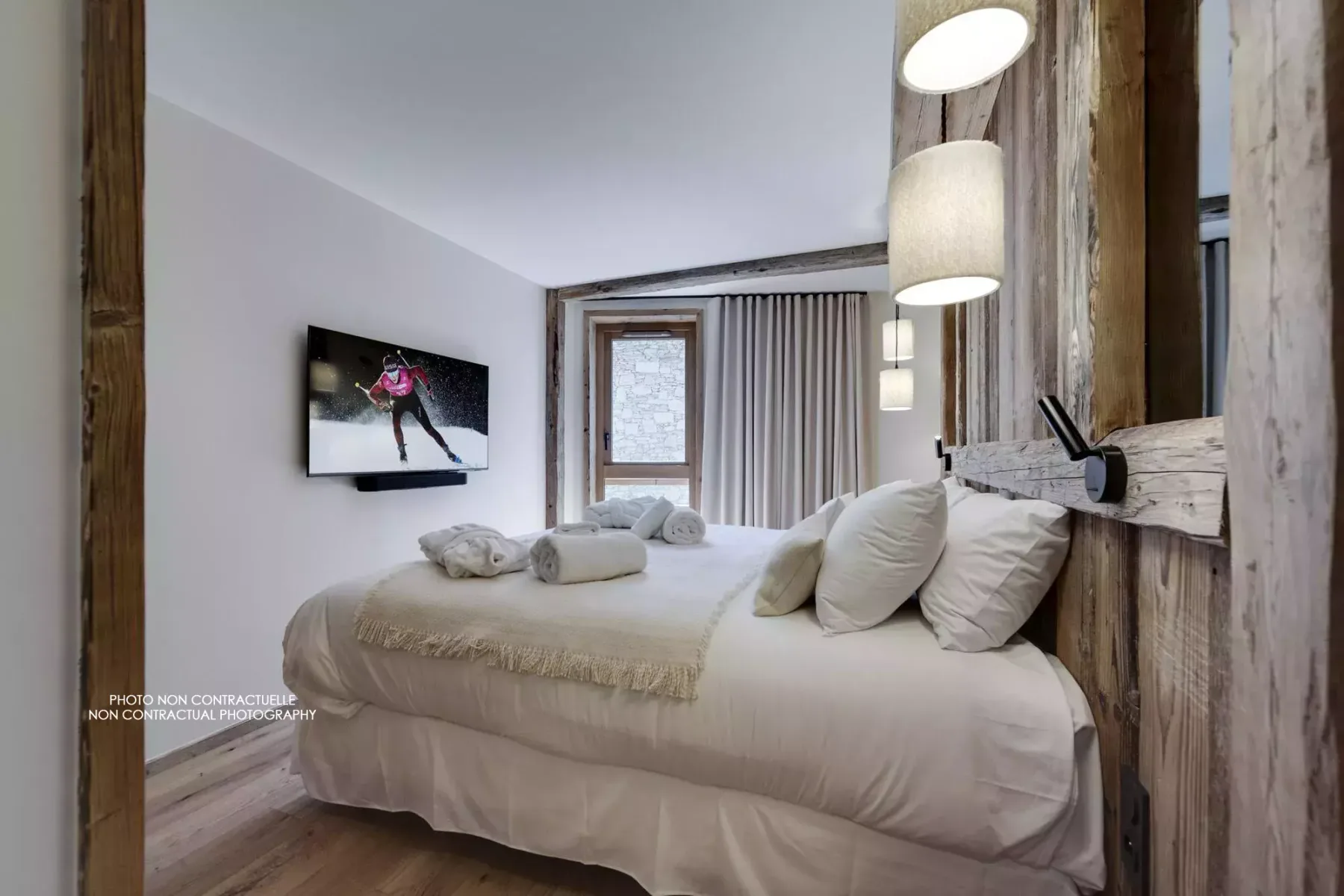 A bedroom with a large bed, neutral bedding, and pendant lights.
