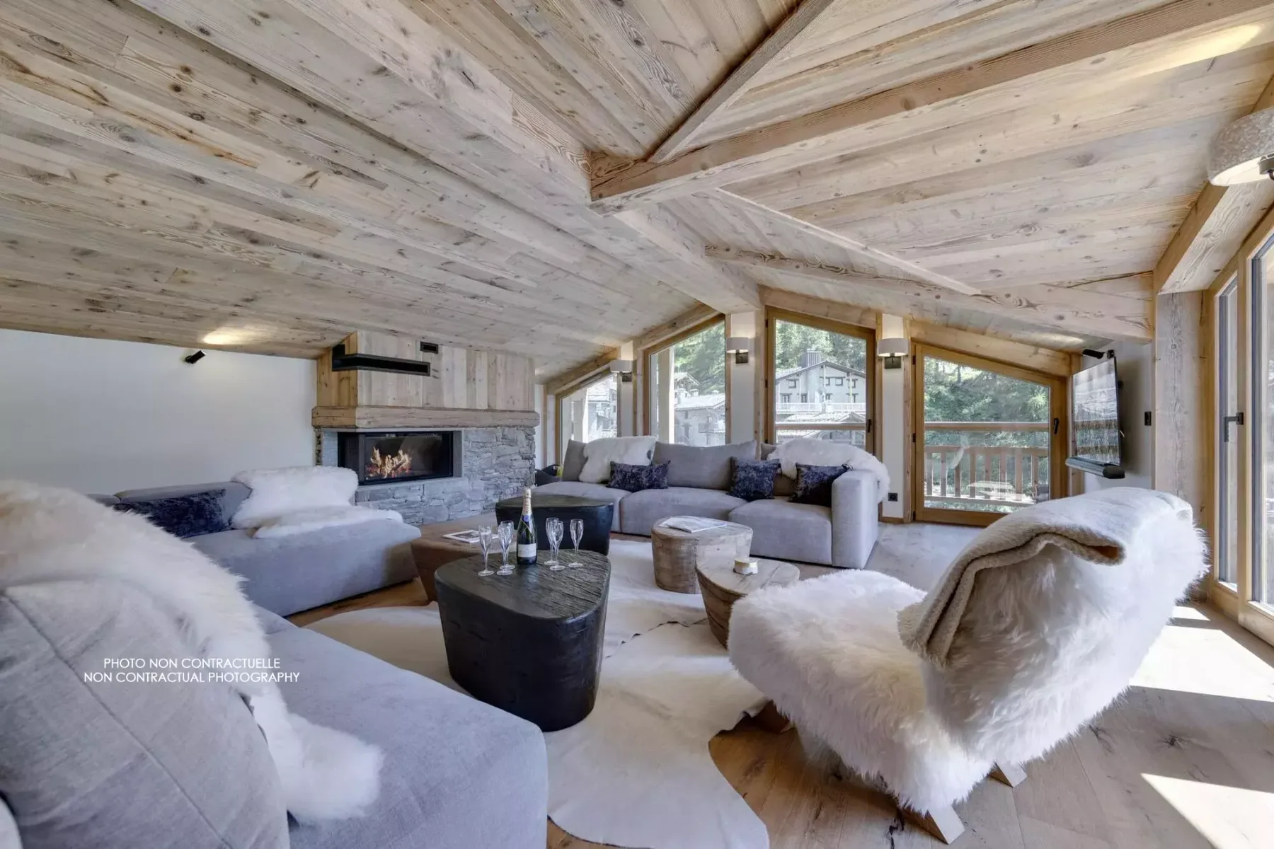 A bright living room with a stone fireplace, broad windows, and seating.