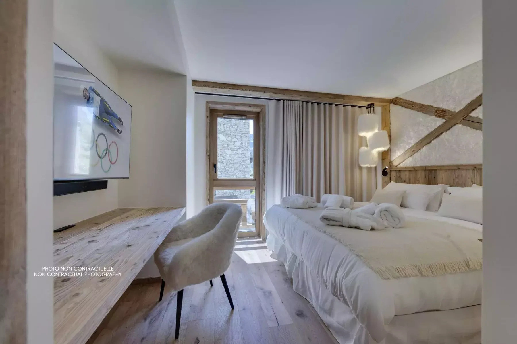 A bedroom with a large bed, a wall-mounted television, and a desk.