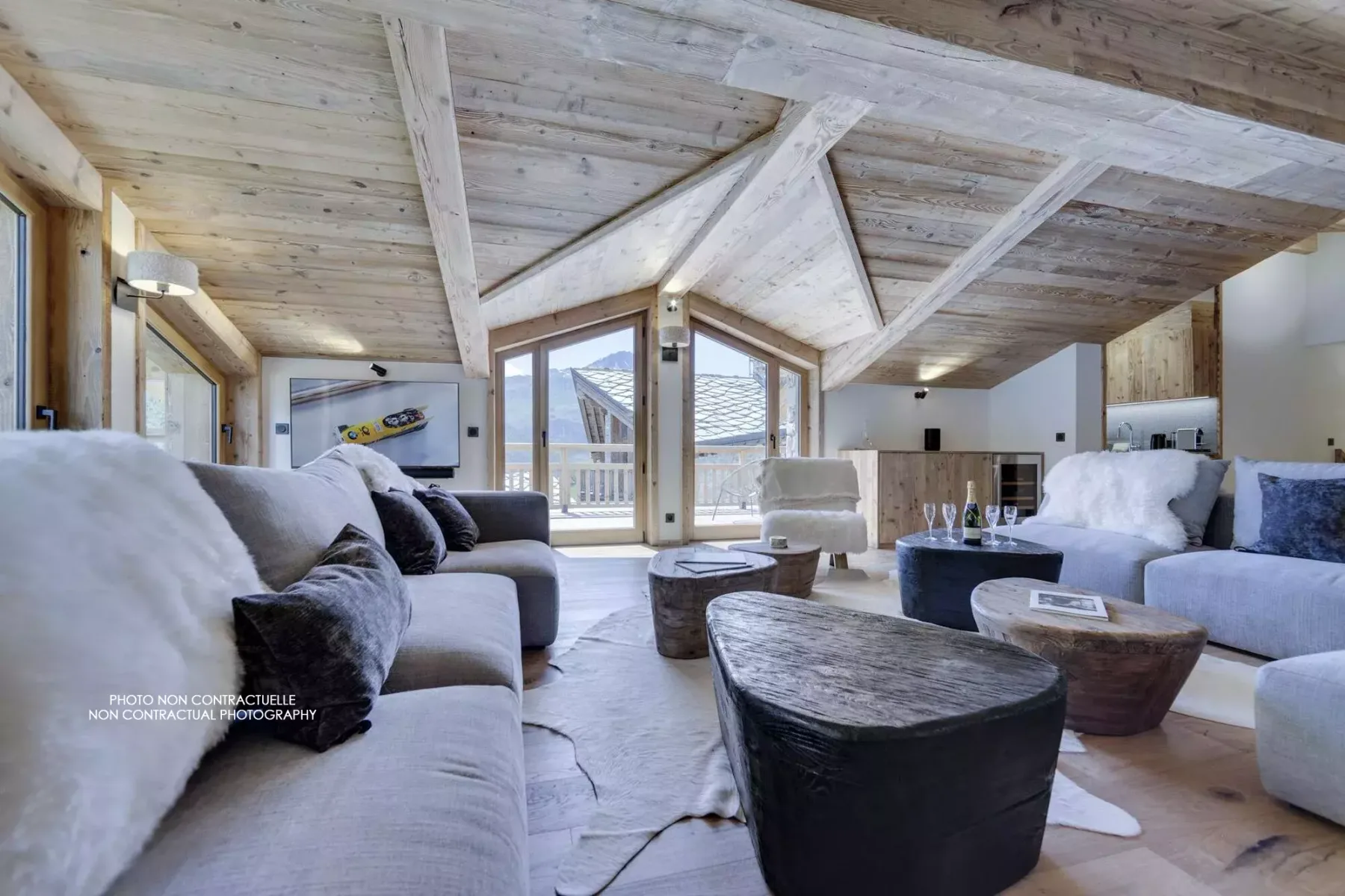 A bright living room with seating and large windows beneath a sloped wooden ceiling.
