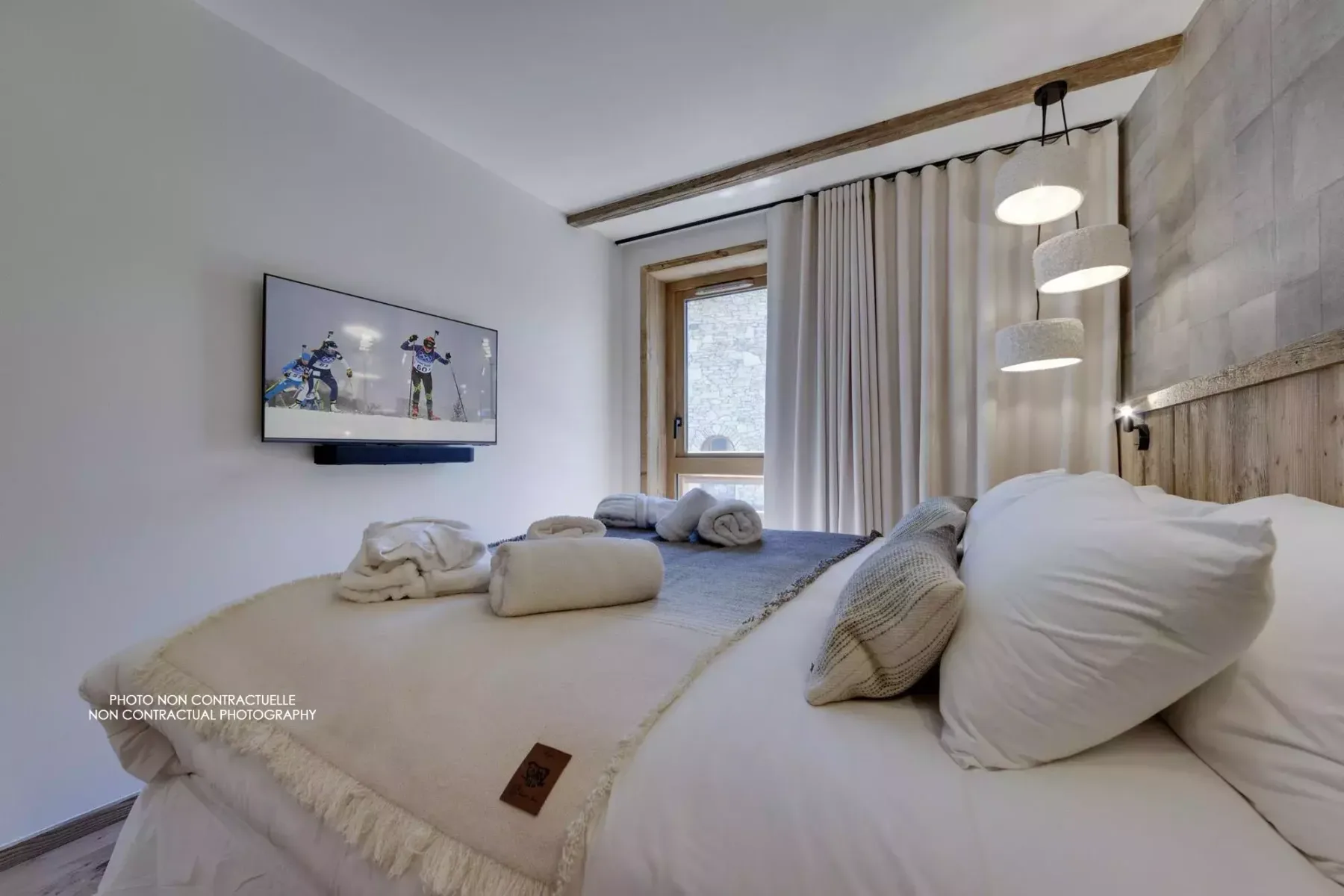 A bedroom with a bed, wall-mounted television, and curtains beside the window.