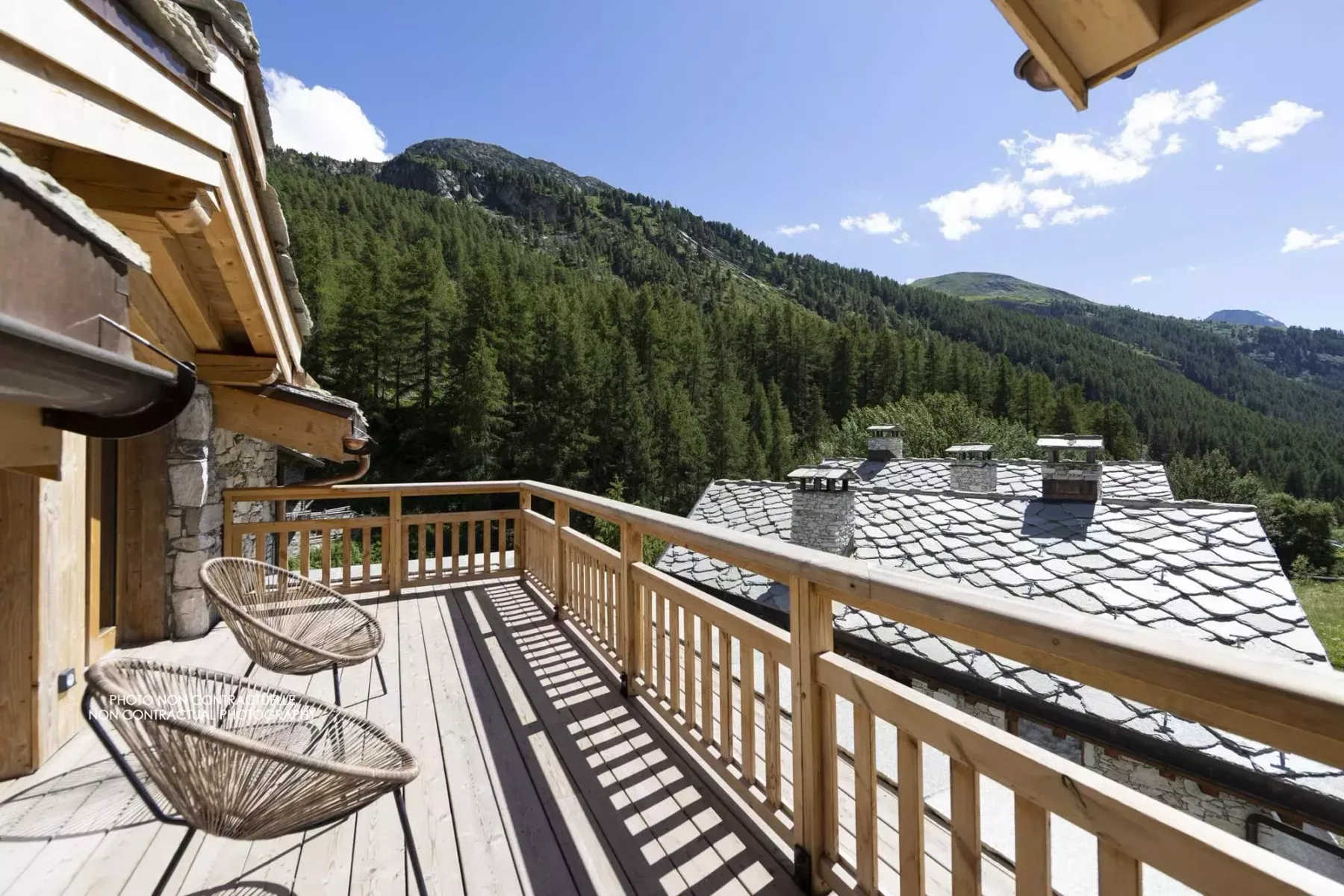 A wooden balcony with seating overlooks forested mountain slopes.