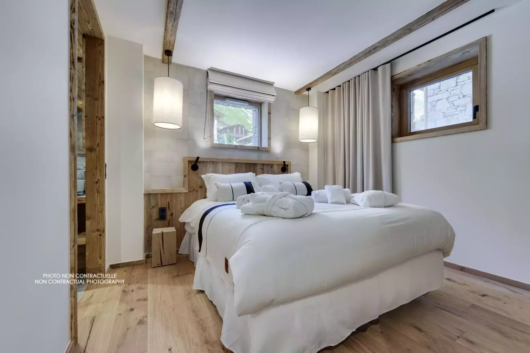 Bedroom with white bedding, wooden beams, and windows beside the bed.