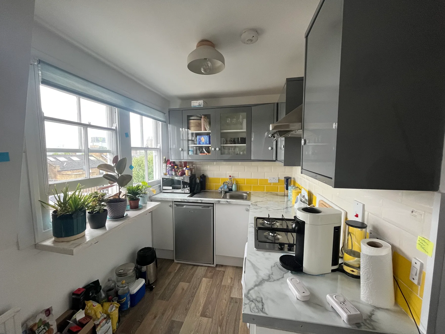 A bright kitchen with gray cabinets, a yellow backsplash, and plants by the window.