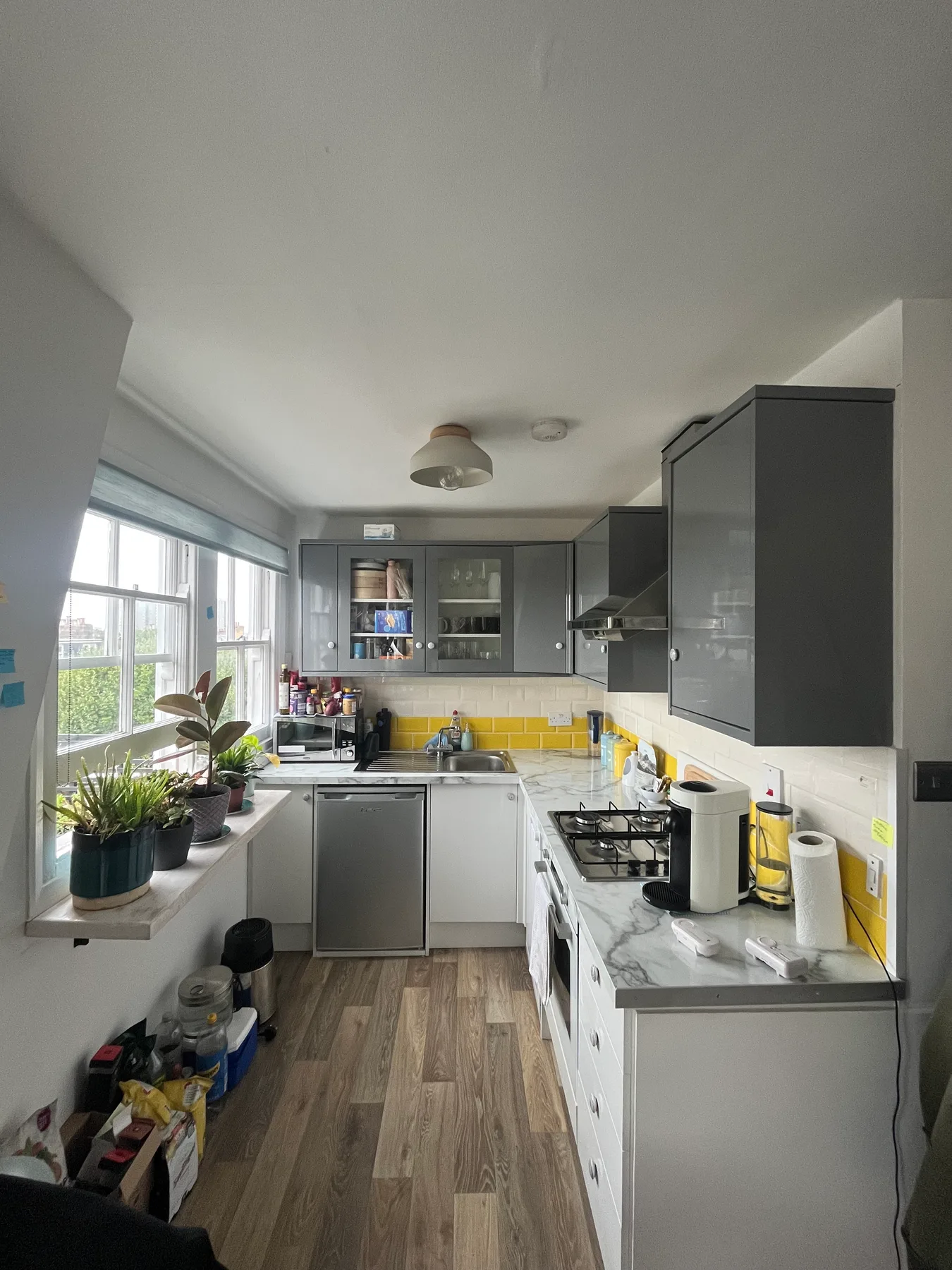 A narrow kitchen with gray cabinets, white counters, and windows along one side.