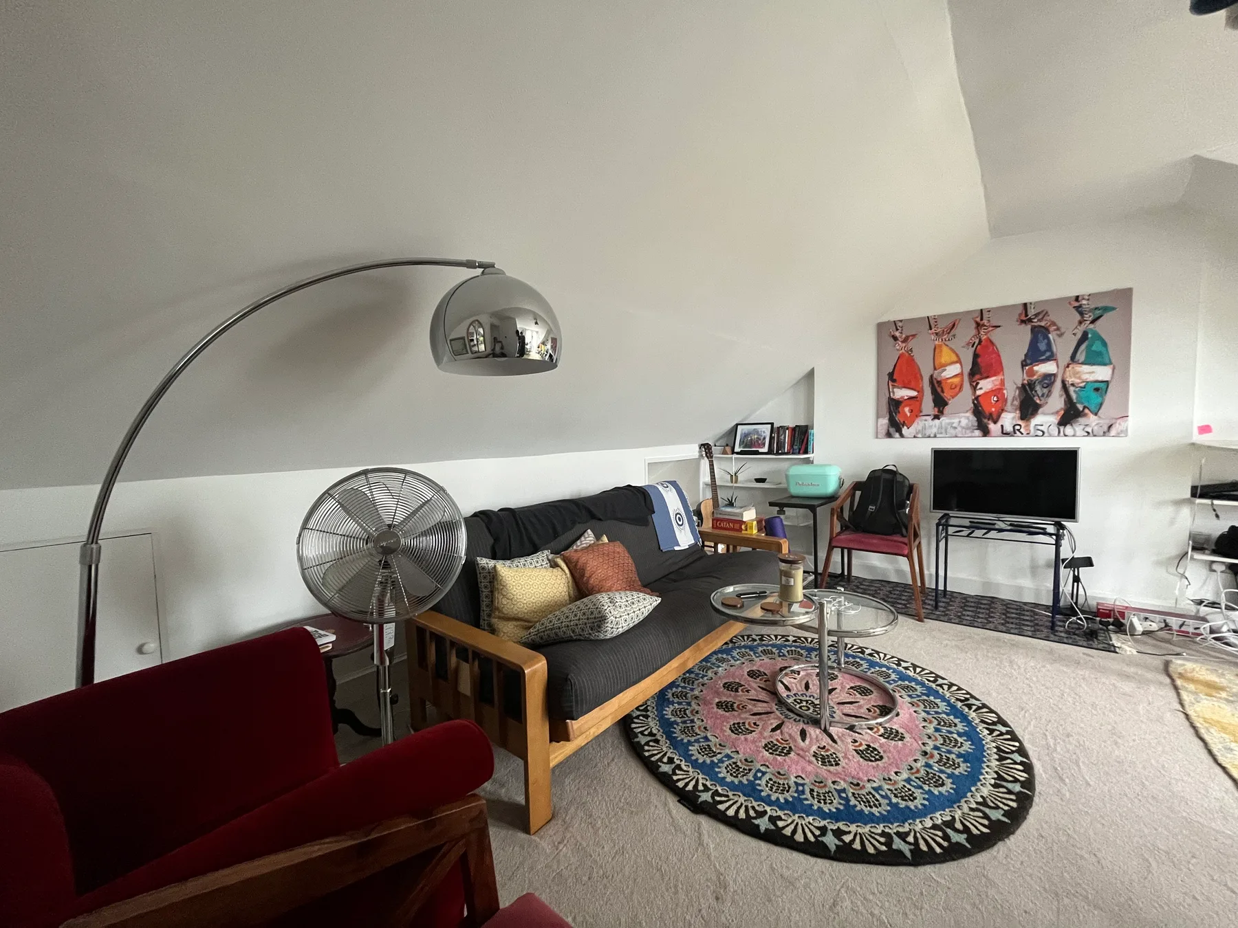 A living room with a wooden seating area, floor fan, and colorful round rug.