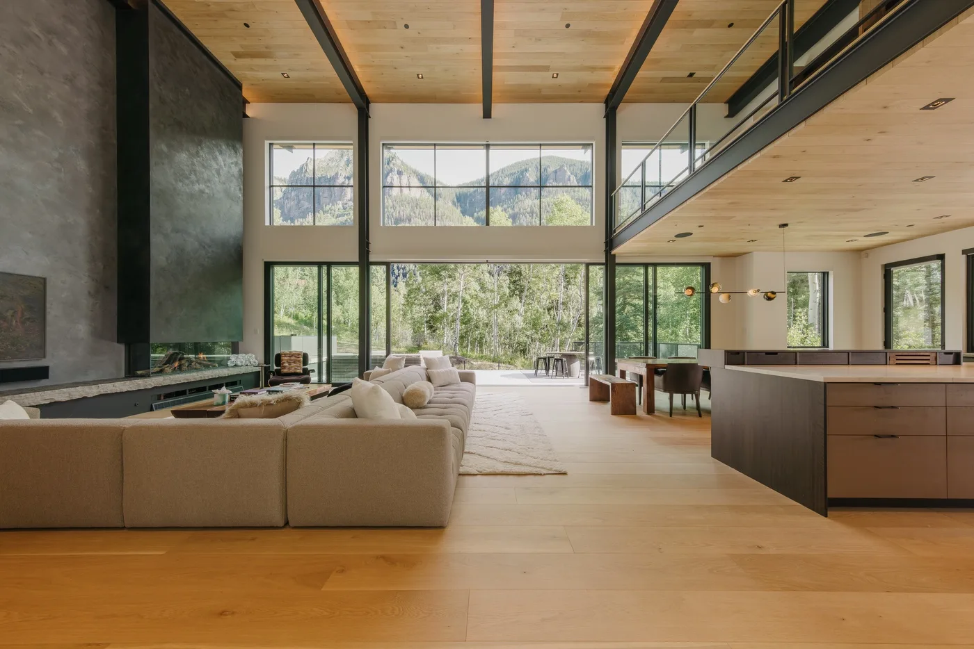 Una amplia sala de estar de concepto abierto con asientos, una isla de cocina y grandes ventanas.