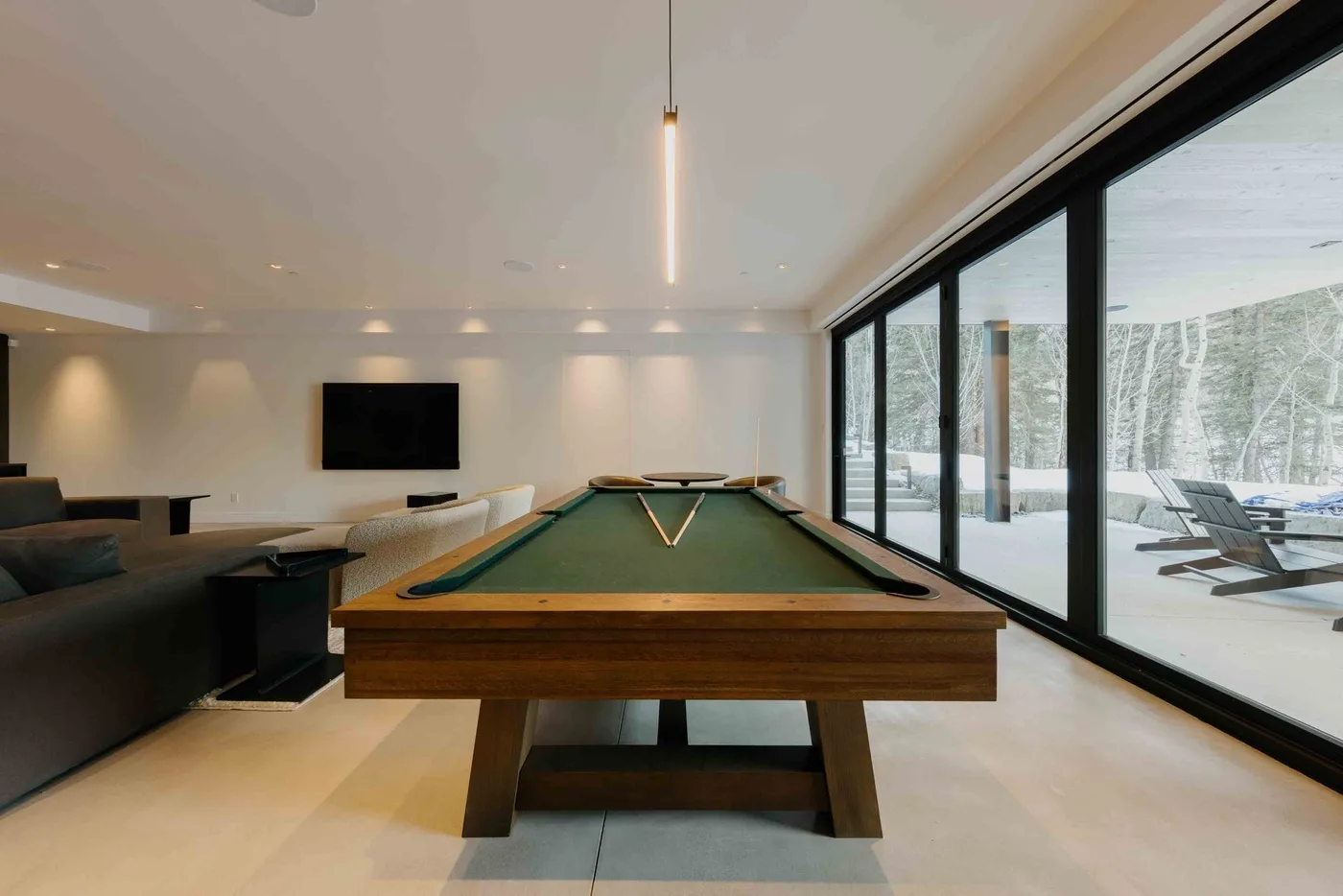 Una mesa de billar ocupa una sala luminosa junto a grandes ventanales.