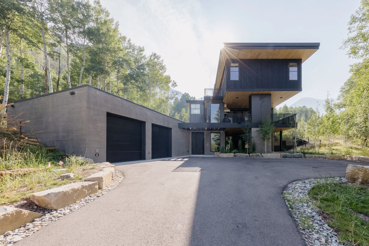 Una casa moderna con una entrada amplia y un garaje para dos autos, rodeada de árboles.