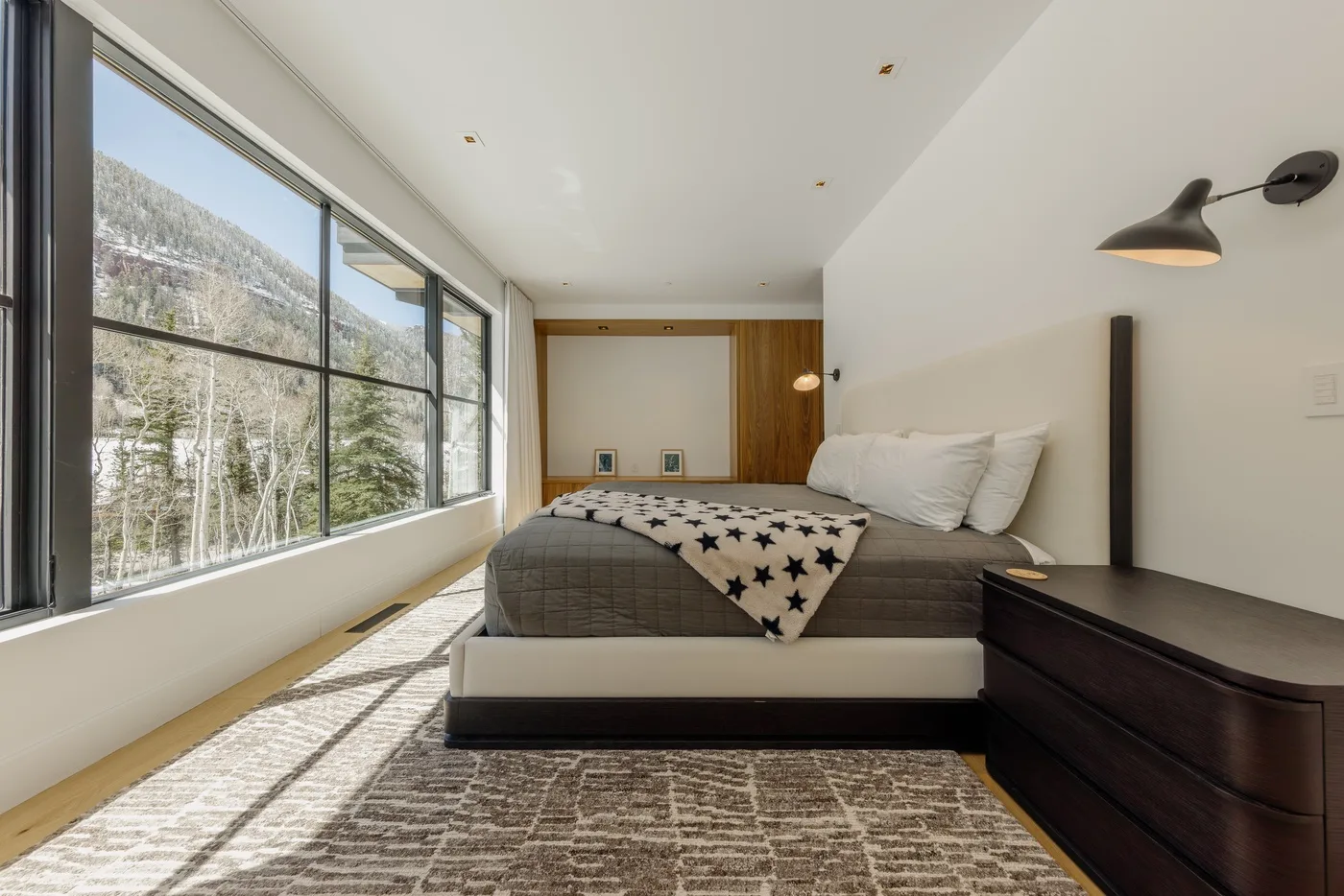 Un dormitorio con una cama baja y grandes ventanas que dan a una ladera arbolada.