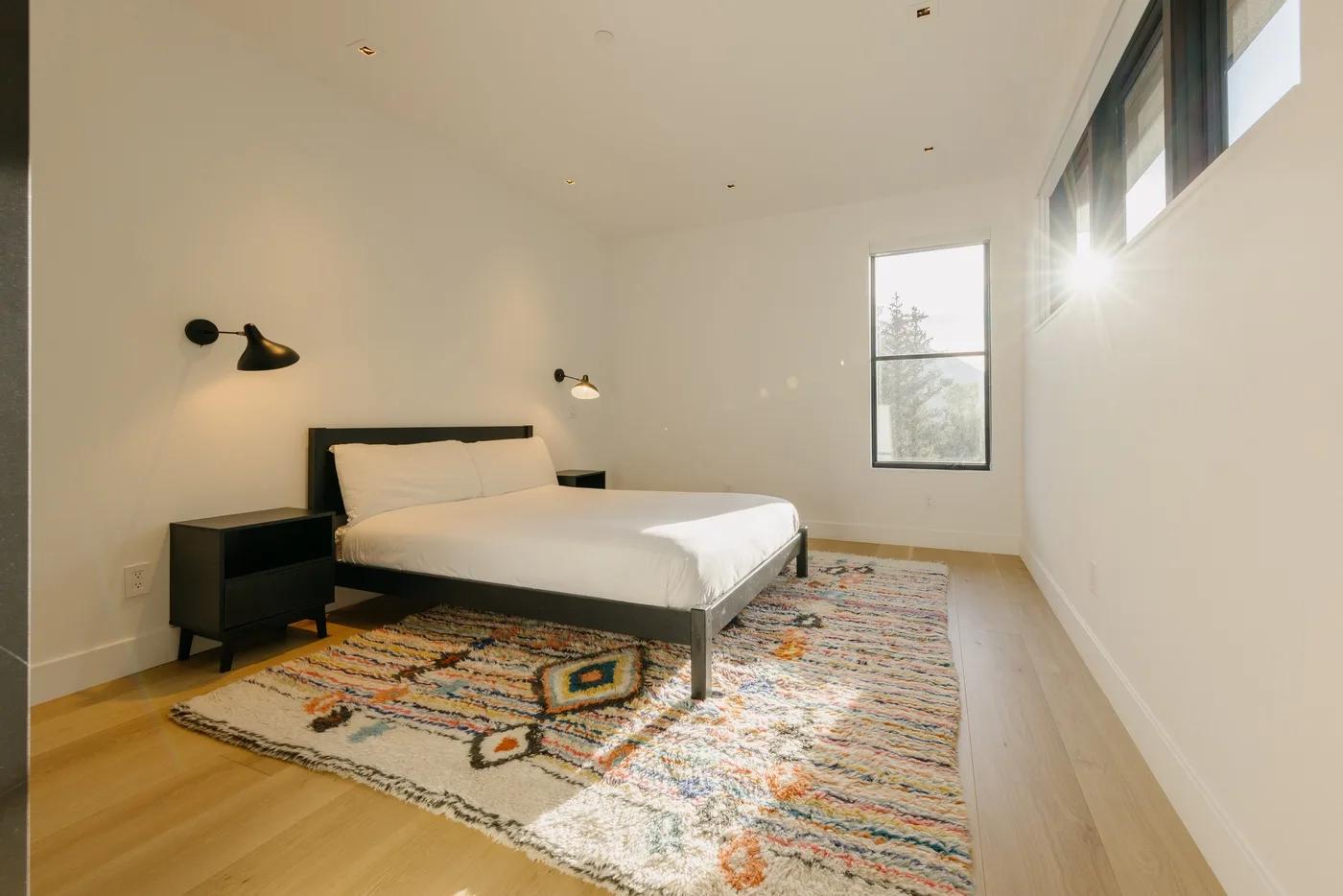 Un dormitorio luminoso con una cama, mesitas de noche y una alfombra estampada.