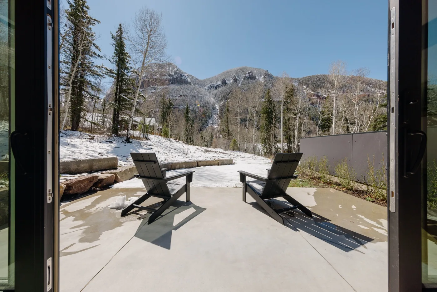 Un patio soleado con dos sillones mira hacia un paisaje montañoso nevado.