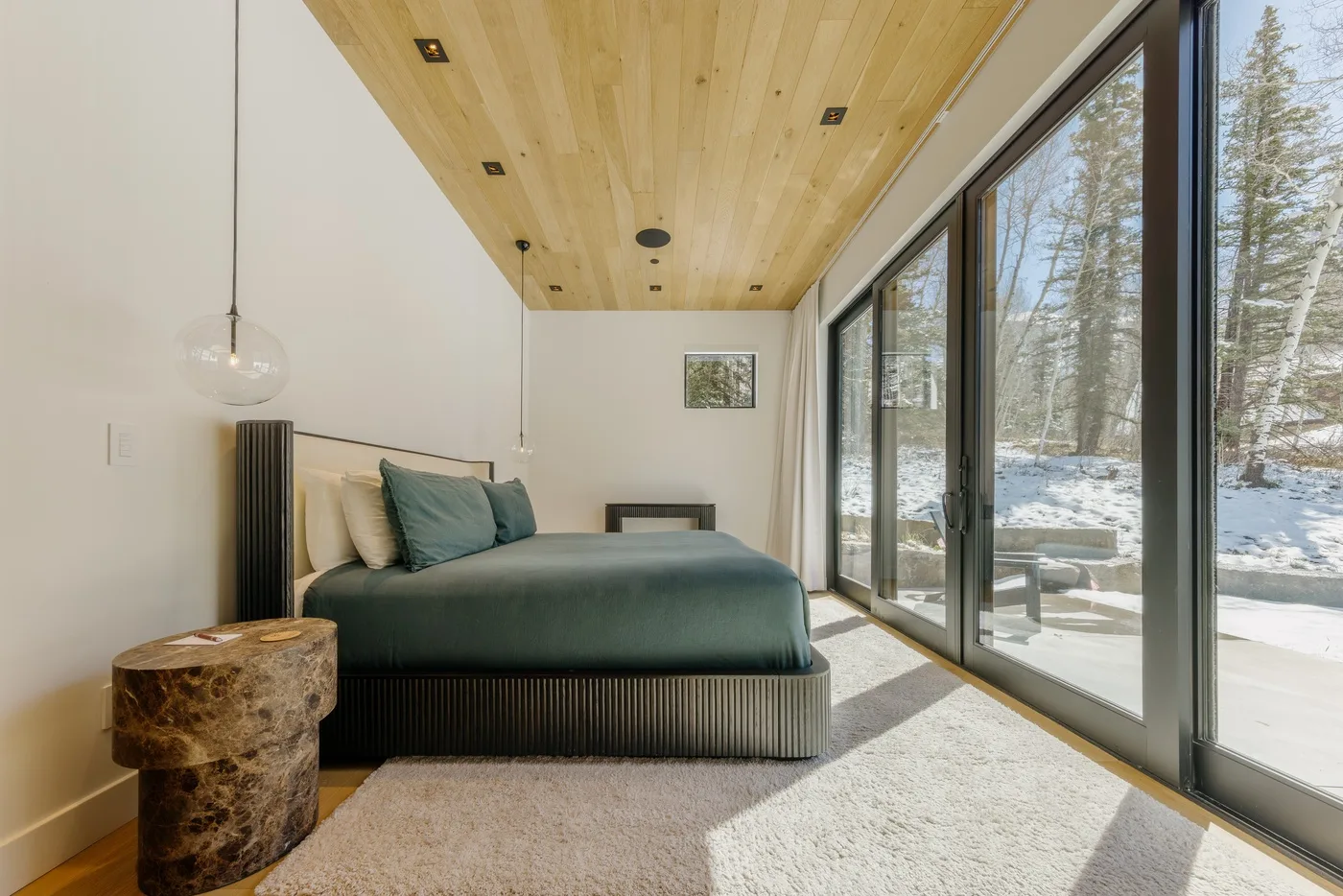 Un dormitorio con una cama junto a grandes ventanales que dan a un paisaje nevado.