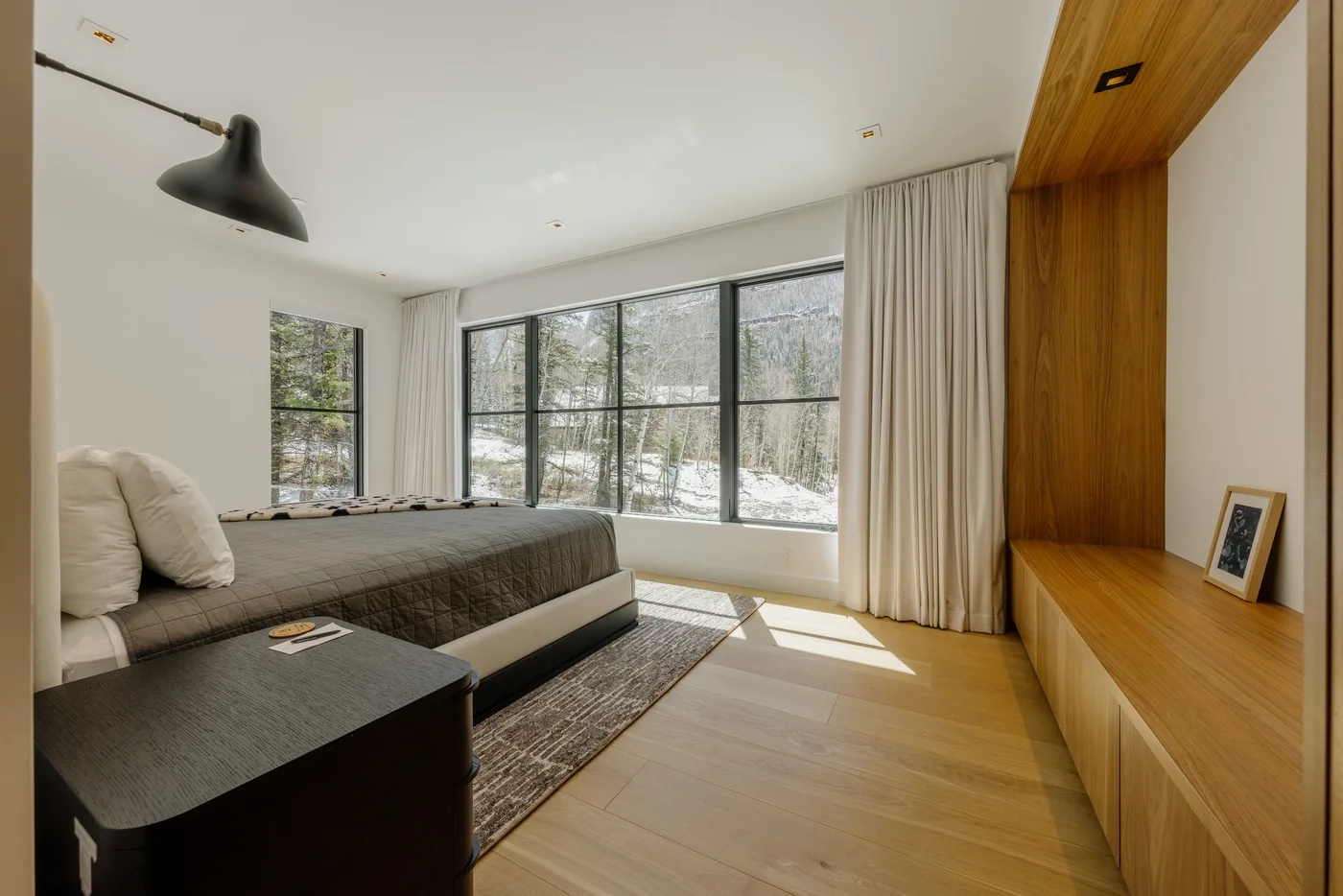 Un dormitorio con una cama junto a grandes ventanas con vistas a los árboles.
