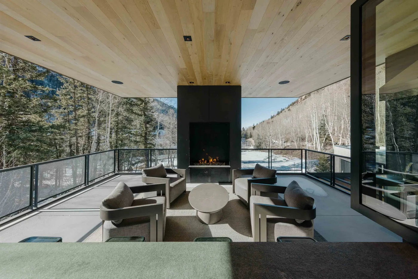 Una sala moderna se abre a una terraza con barandilla de vidrio y vistas al bosque y las montañas.