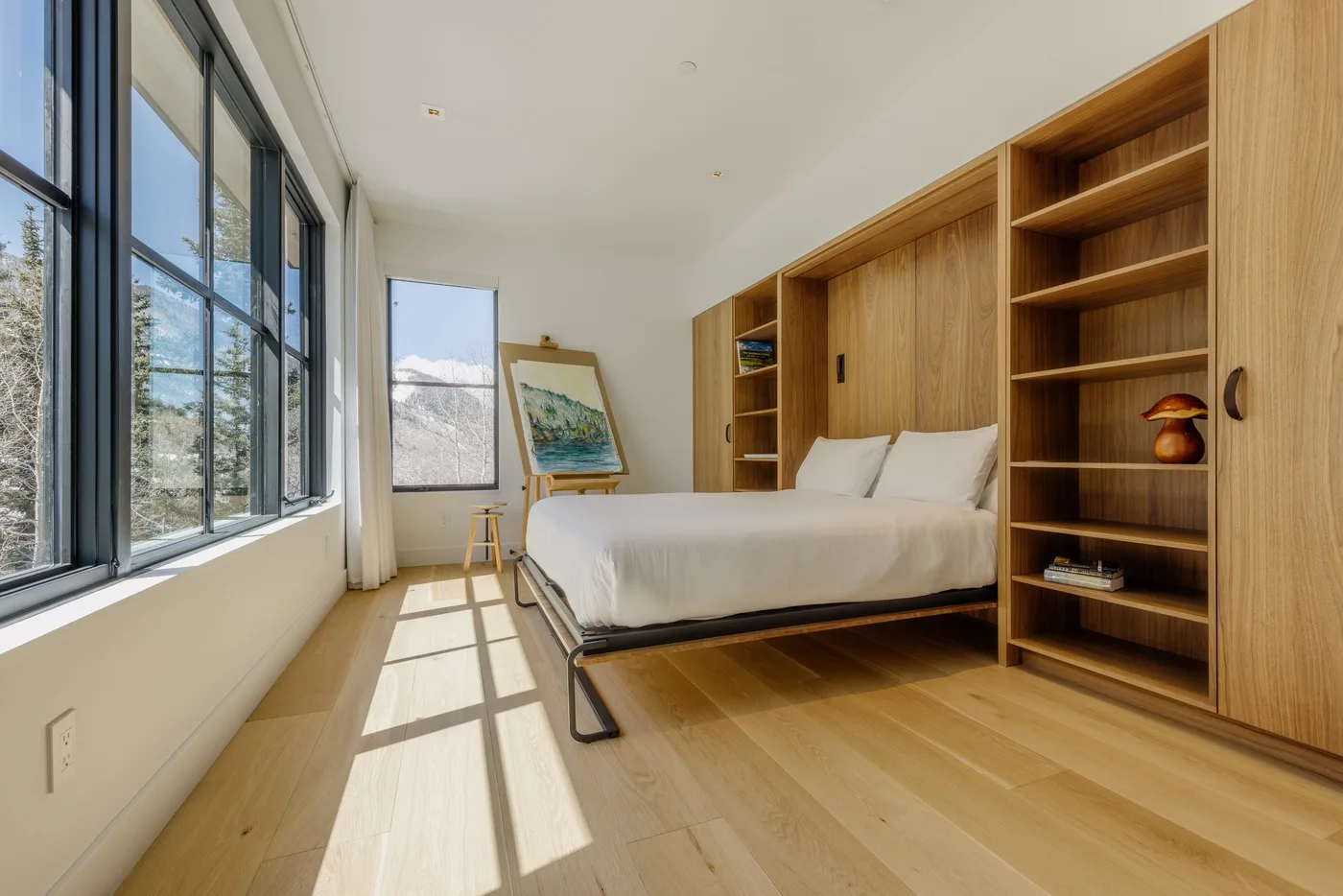 Un dormitorio con una cama junto a estanterías de madera empotradas y grandes ventanas.