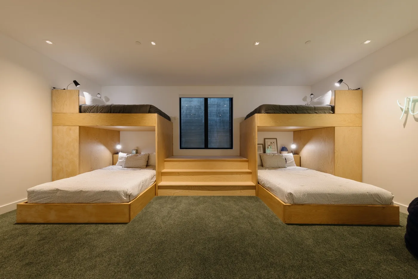 Un dormitorio con dos camas bajas, plataformas elevadas para dormir y una ventana central.