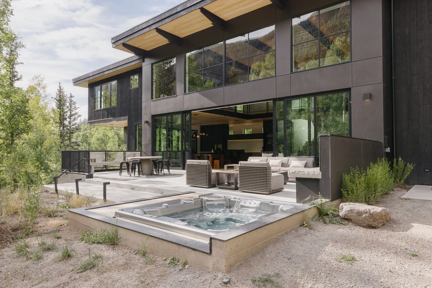 Una casa moderna da a un patio con asientos al aire libre y una bañera de hidromasaje.