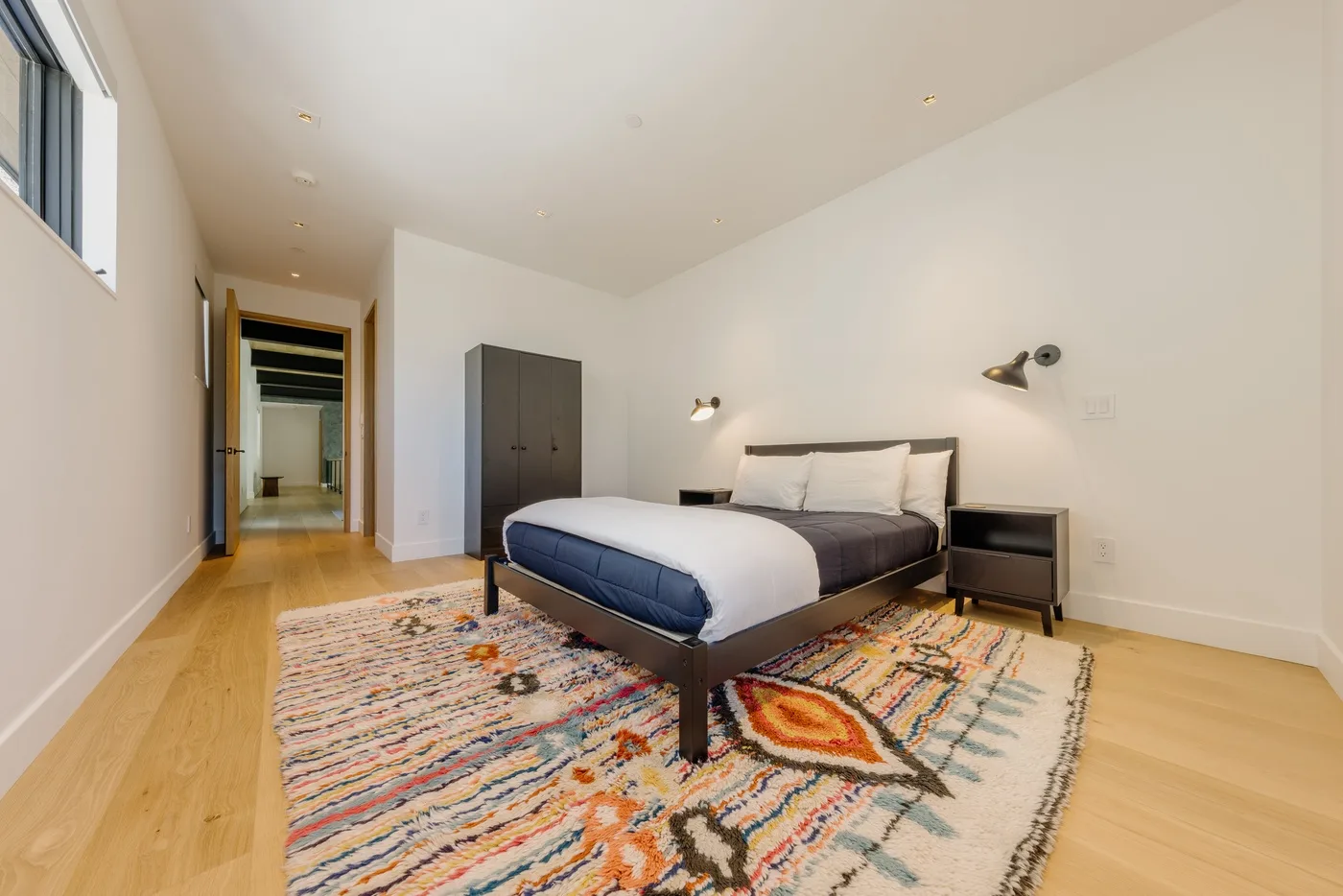 Un dormitorio luminoso con una cama, mesas de noche y una alfombra estampada colorida.