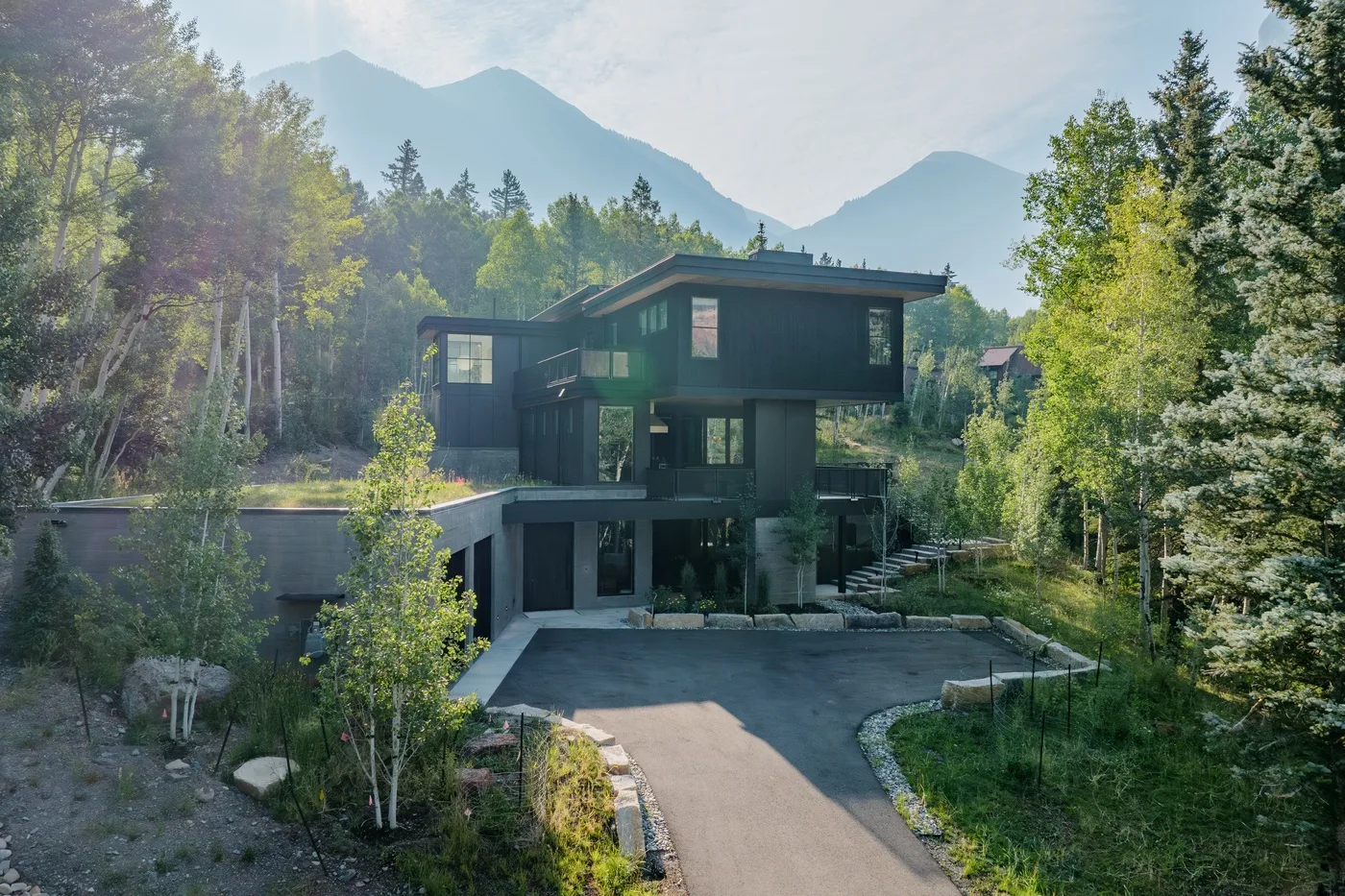 Una casa moderna está rodeada de árboles, con montañas al fondo.