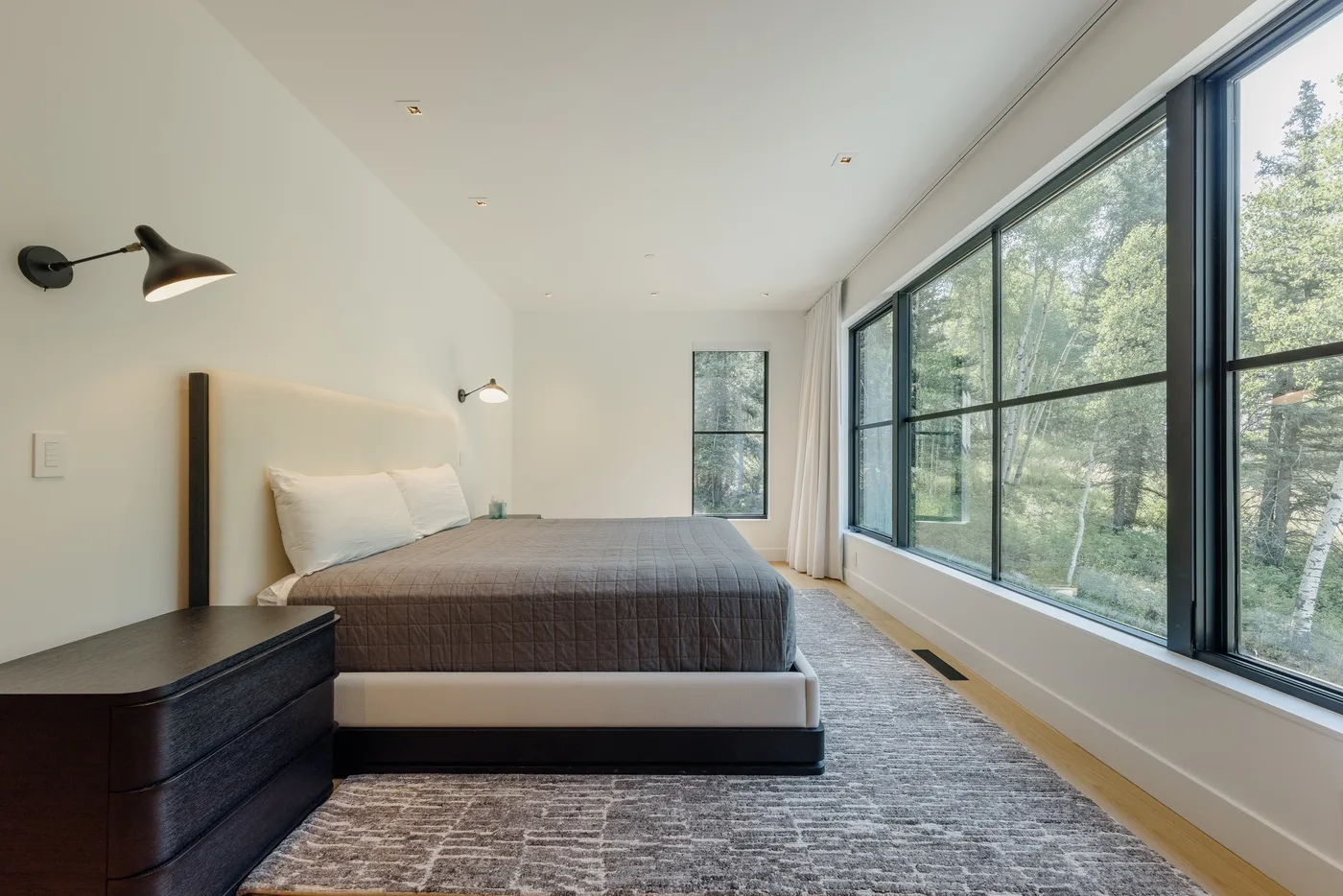 Un dormitorio con una cama grande junto a ventanales con vistas a los árboles.