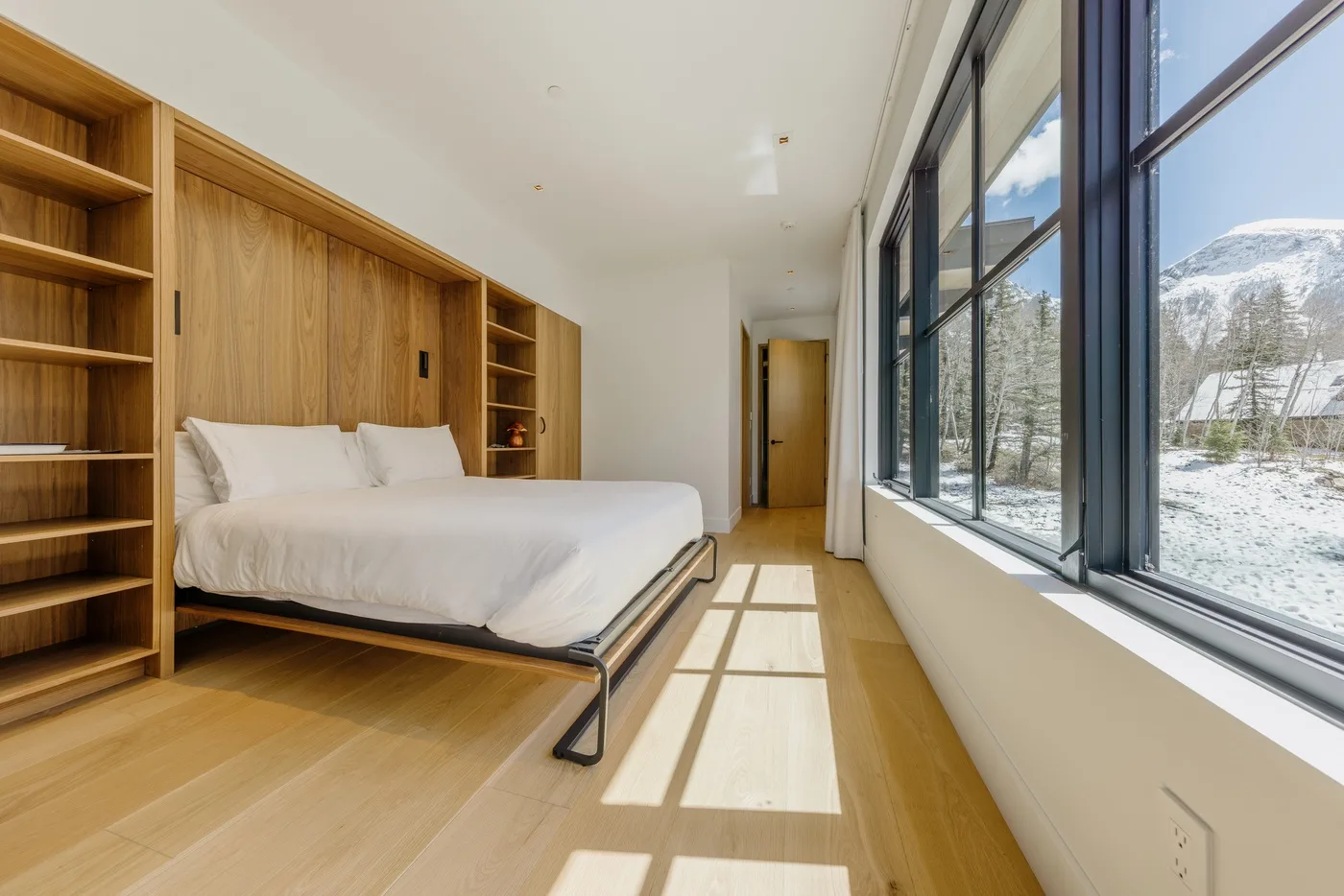 Un dormitorio con una cama junto a grandes ventanas con vistas a un paisaje nevado.