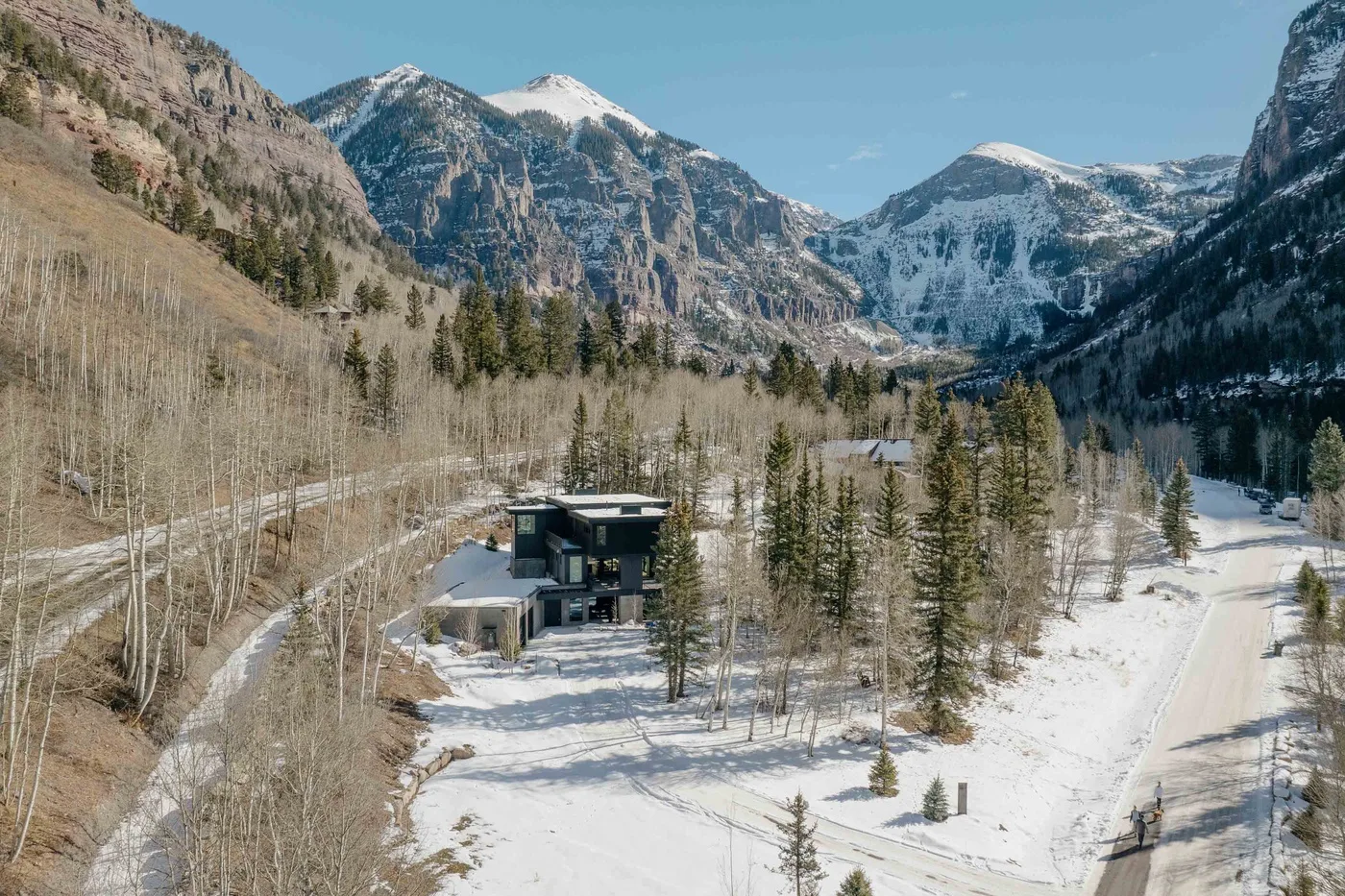 Una casa moderna se encuentra en un valle montañoso nevado entre árboles.